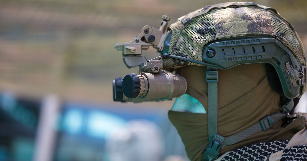 A person wearing military gear that covers their face looks through a pair of night vision binoculars.