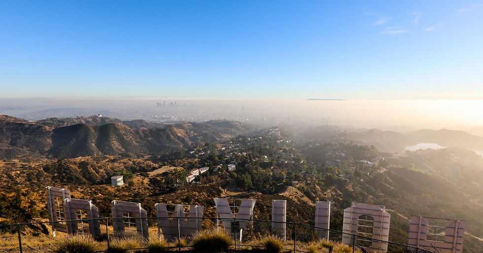 A view from the top of a hill behind the Hollywood sign of downtown LA and the Hollywood hills on a sunny day.