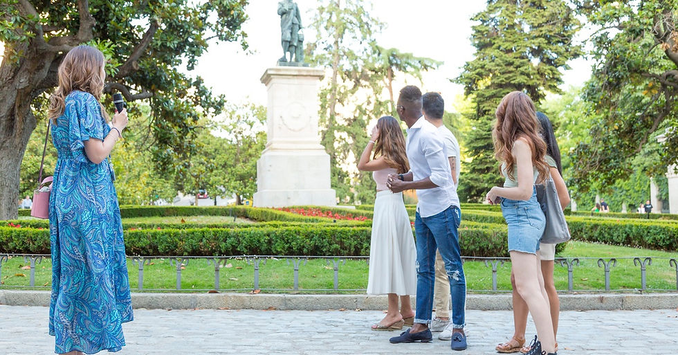 A young woman wearing a blue dress holding a microphone, standing in front of five people looking at a statue.