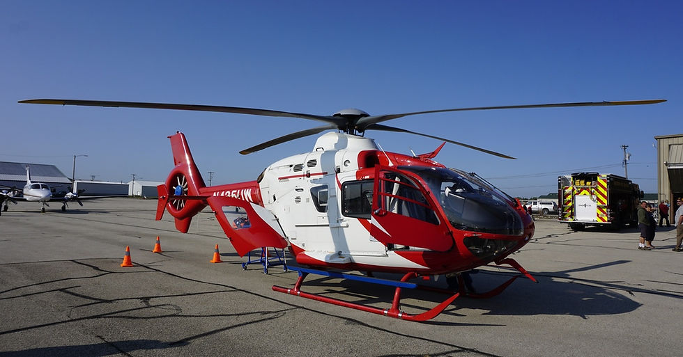 A red and white ambulance helicopter parked on a cemented runway with orange traffic cones behind it.