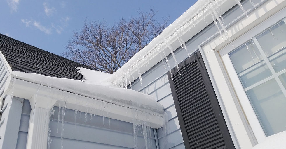 A blue home that has icicles forming on the edge of white gutters while the snow piles up on them.