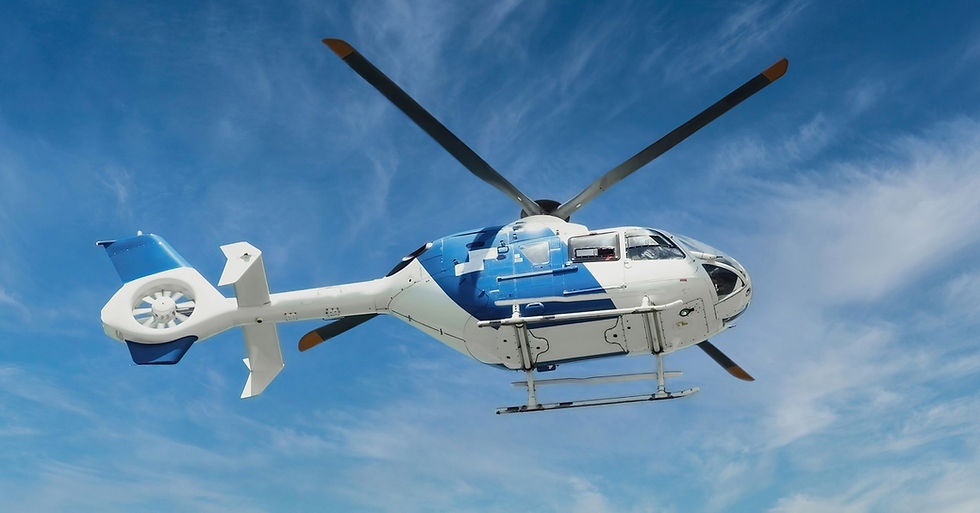 A blue and white medical emergency helicopter is mid-air, behind it are clear, bright blue skies.