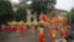Performers in colorful attire maneuver a vibrant dragon costume in a festive parade. Onlookers watch near a historic building.