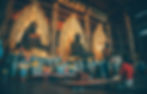 Ornate golden Buddha statues in a temple. People kneel and pray with offerings. Intricate carvings and warm lighting create a serene mood.