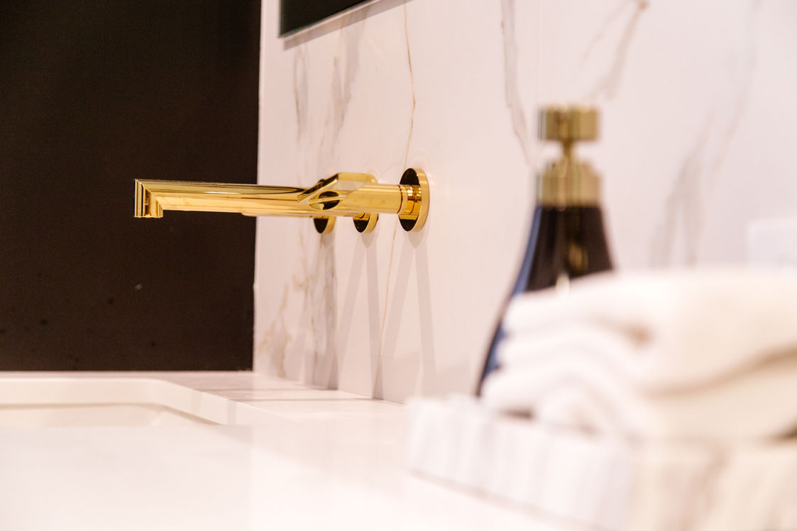 Modern gold wall-mounted faucet in a marble bathroom