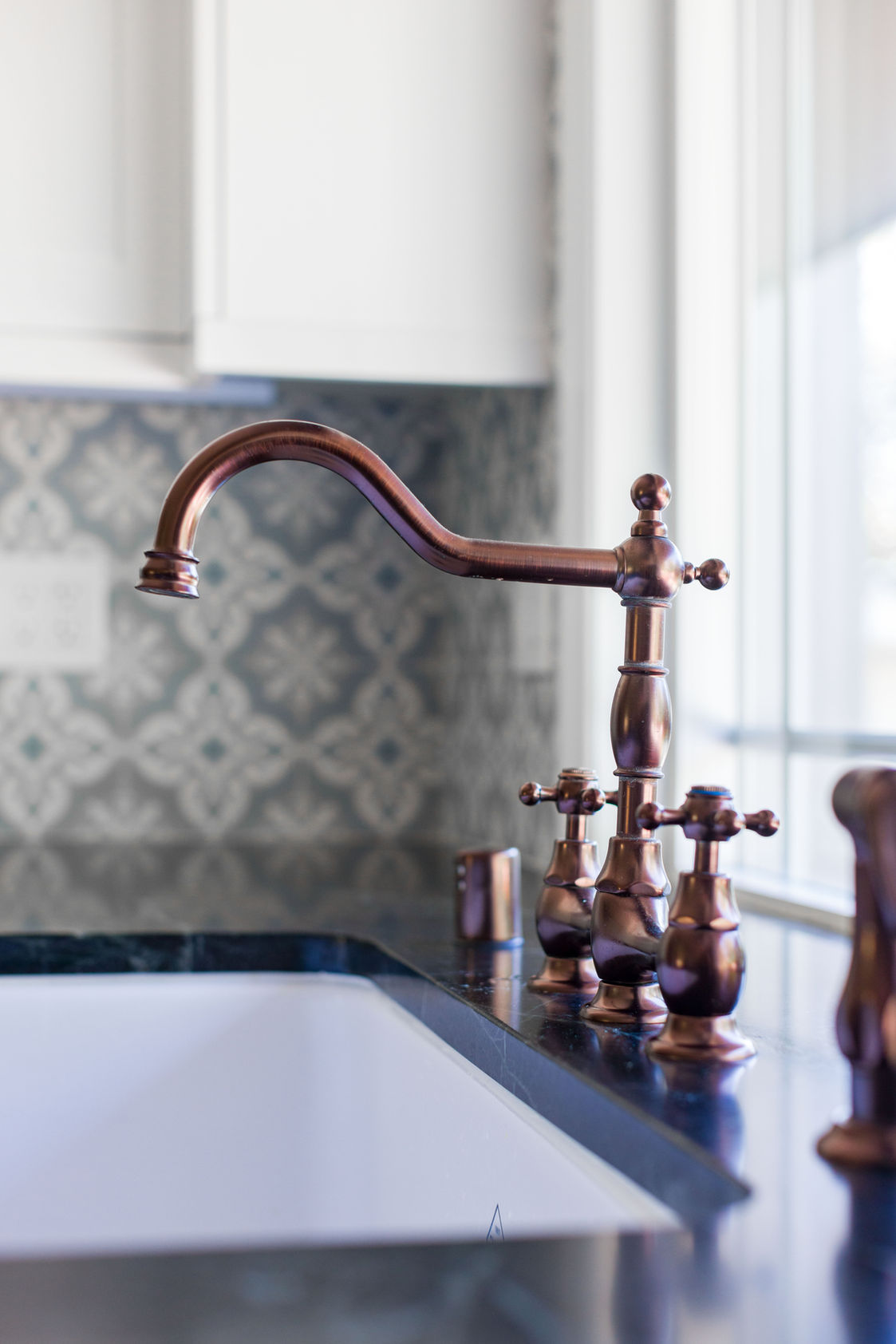 Copper kitchen faucet with ornate handles and patterned backsplash.