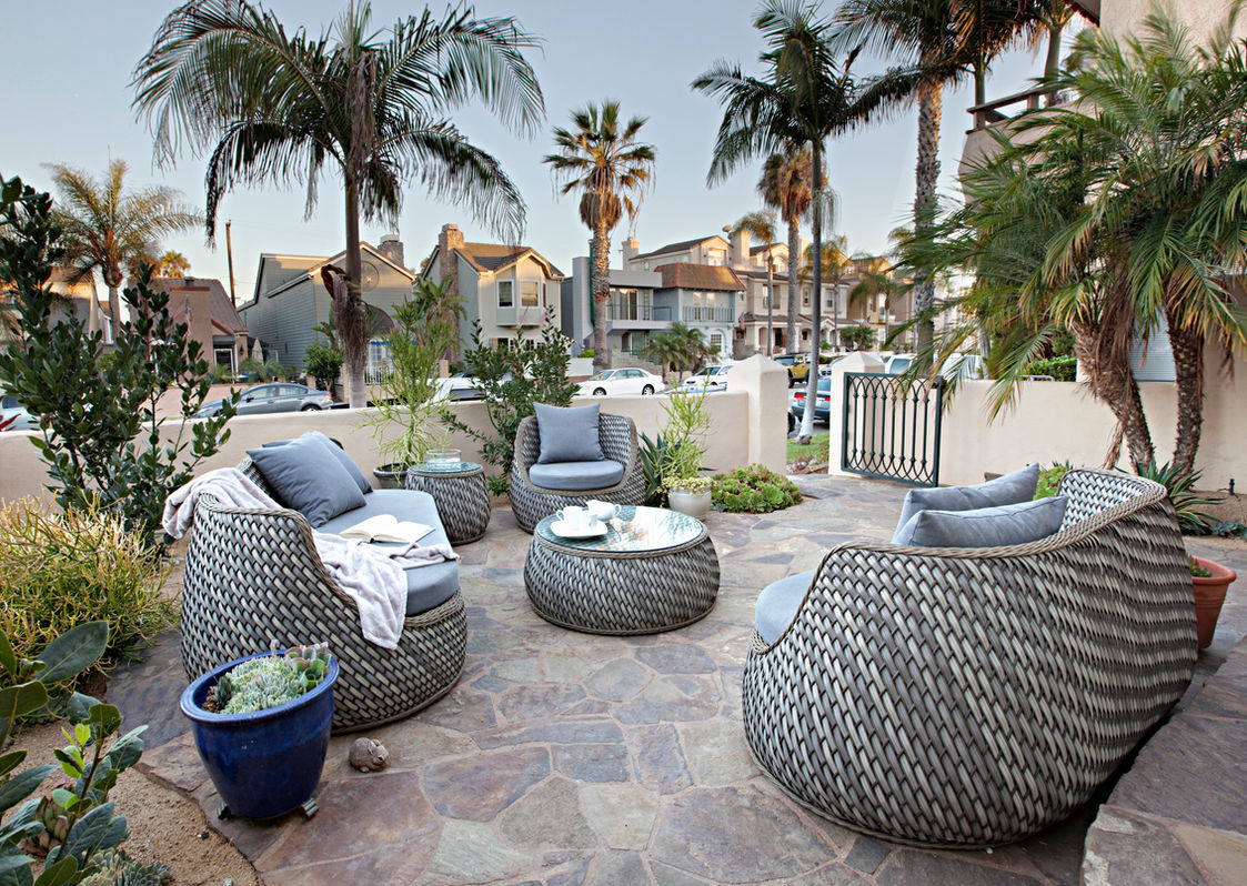 Modern wicker patio furniture on a stone terrace with palms.