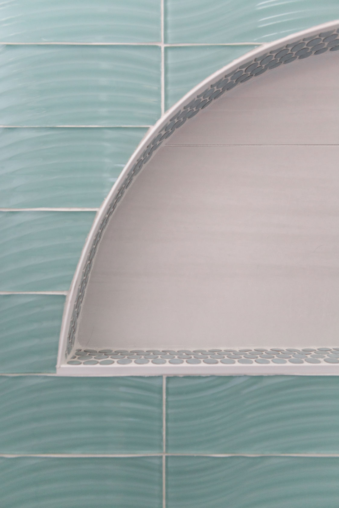 Curved white bathroom shelf against teal wavy tiles
