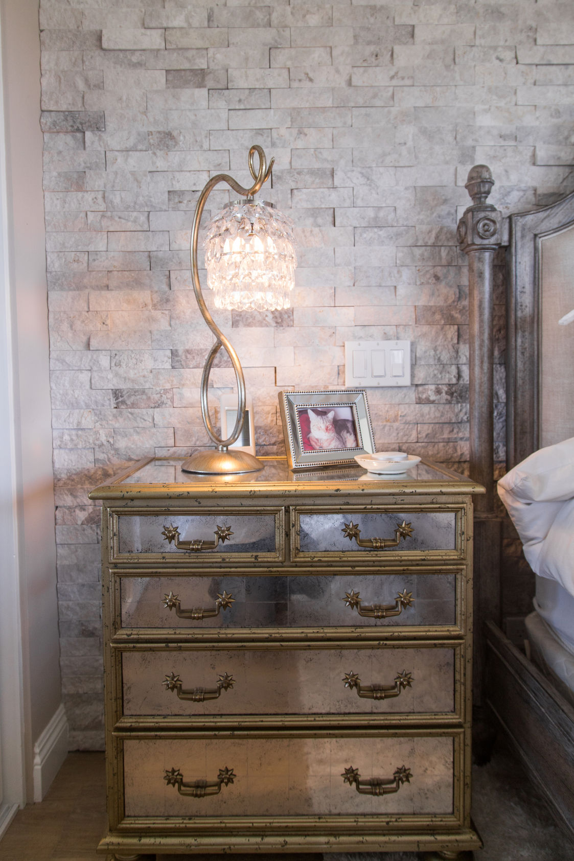Mirrored nightstand with crystal lamp and stone wall.
