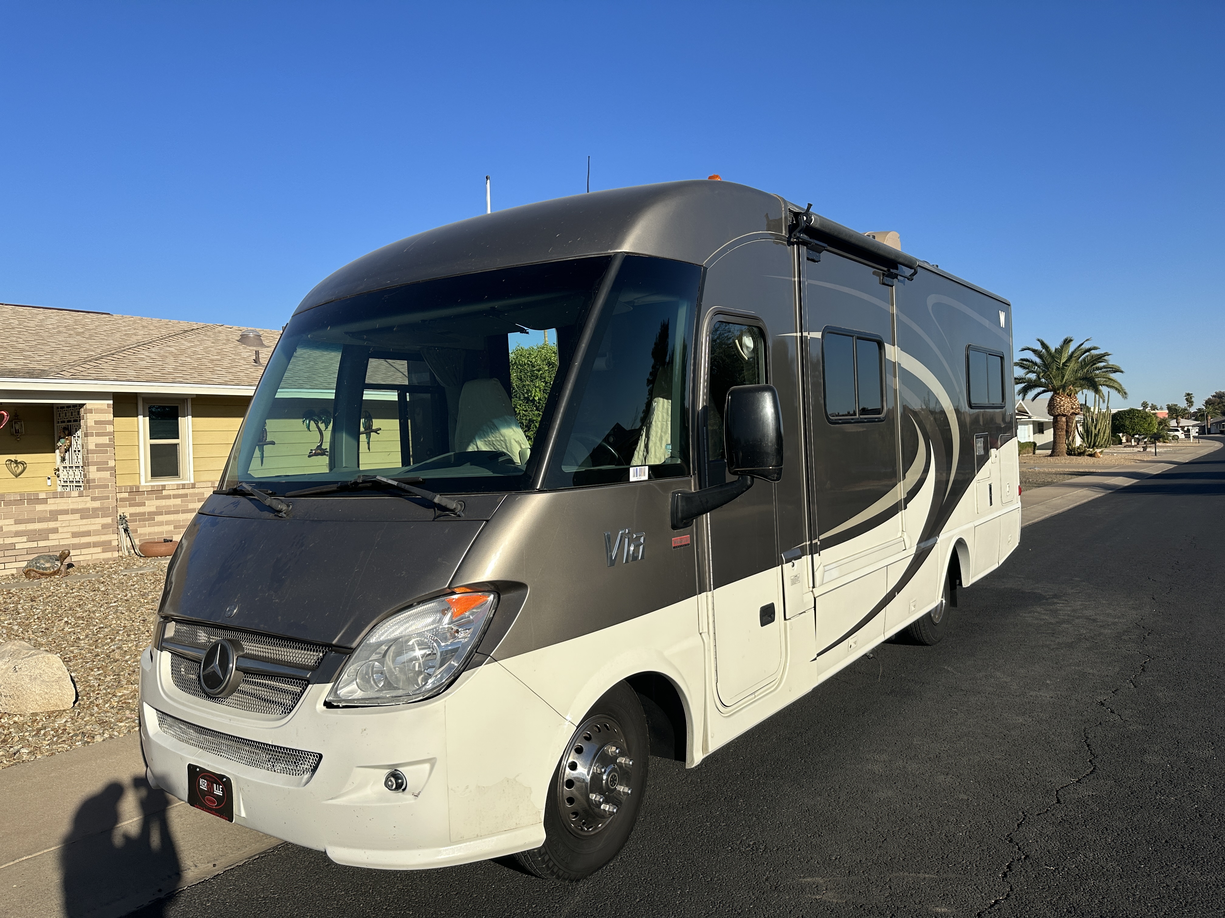 Motorhome parked outdoors with its front windshield, entry side and exterior compartments visible