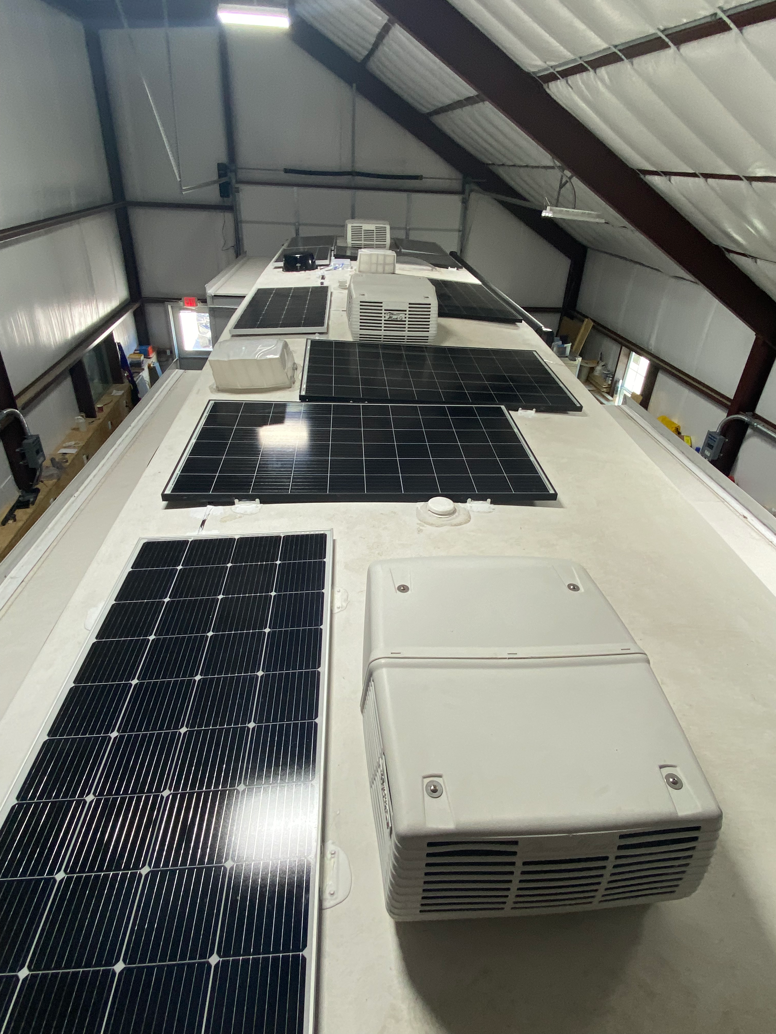 RV rooftop with solar panels, air-conditioning equipment and roof openings inside a workshop