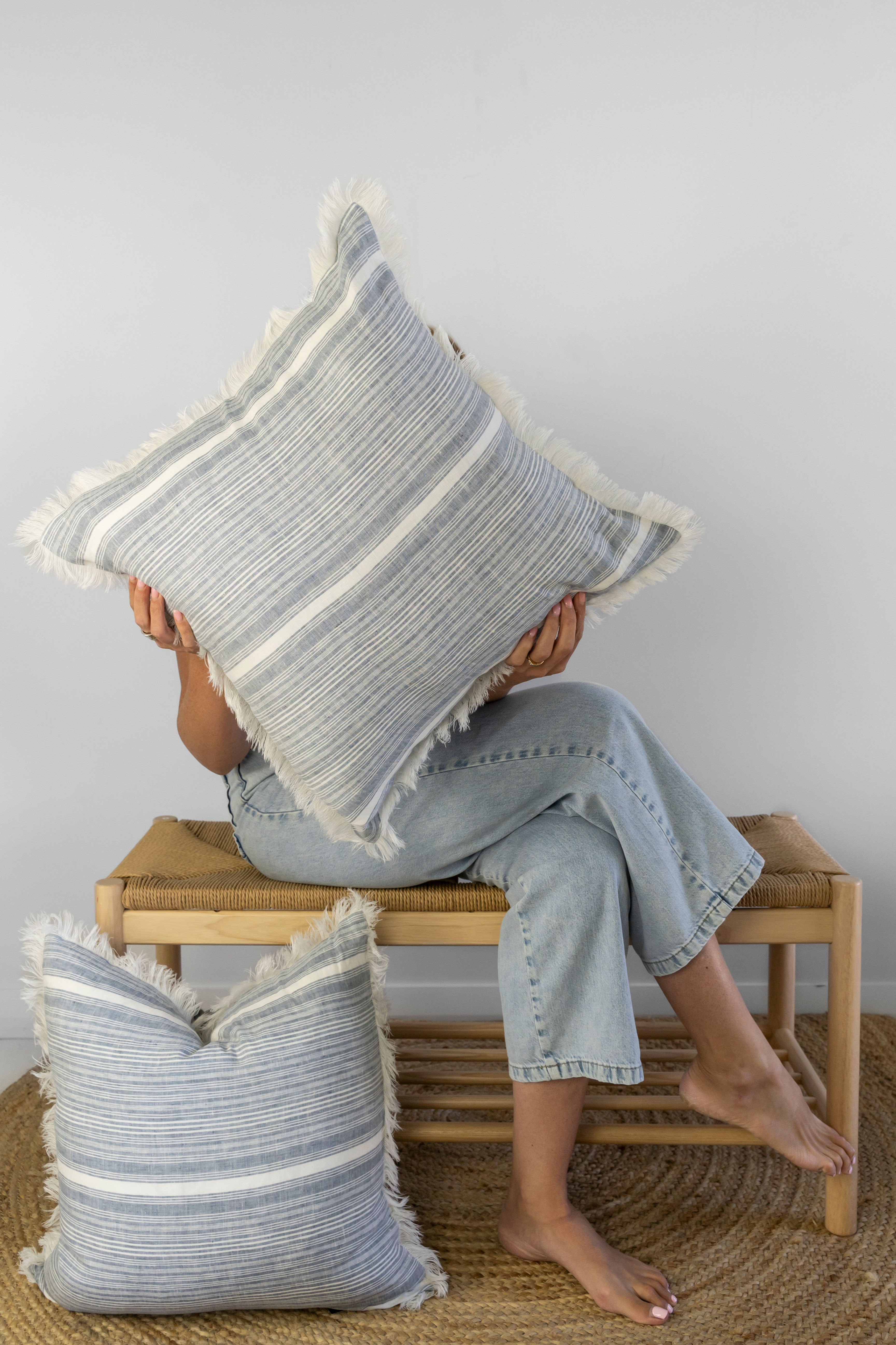Denim blue striped 100% linen cushion held by a girl sitting on a rattan bench.
