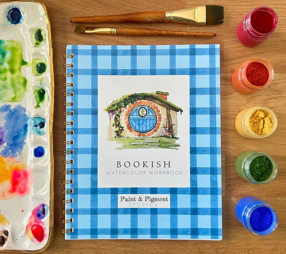 Book with blue gingham edges depicting a hobbit house with a blue door is sitting on a table with rainbow paints and brushes.