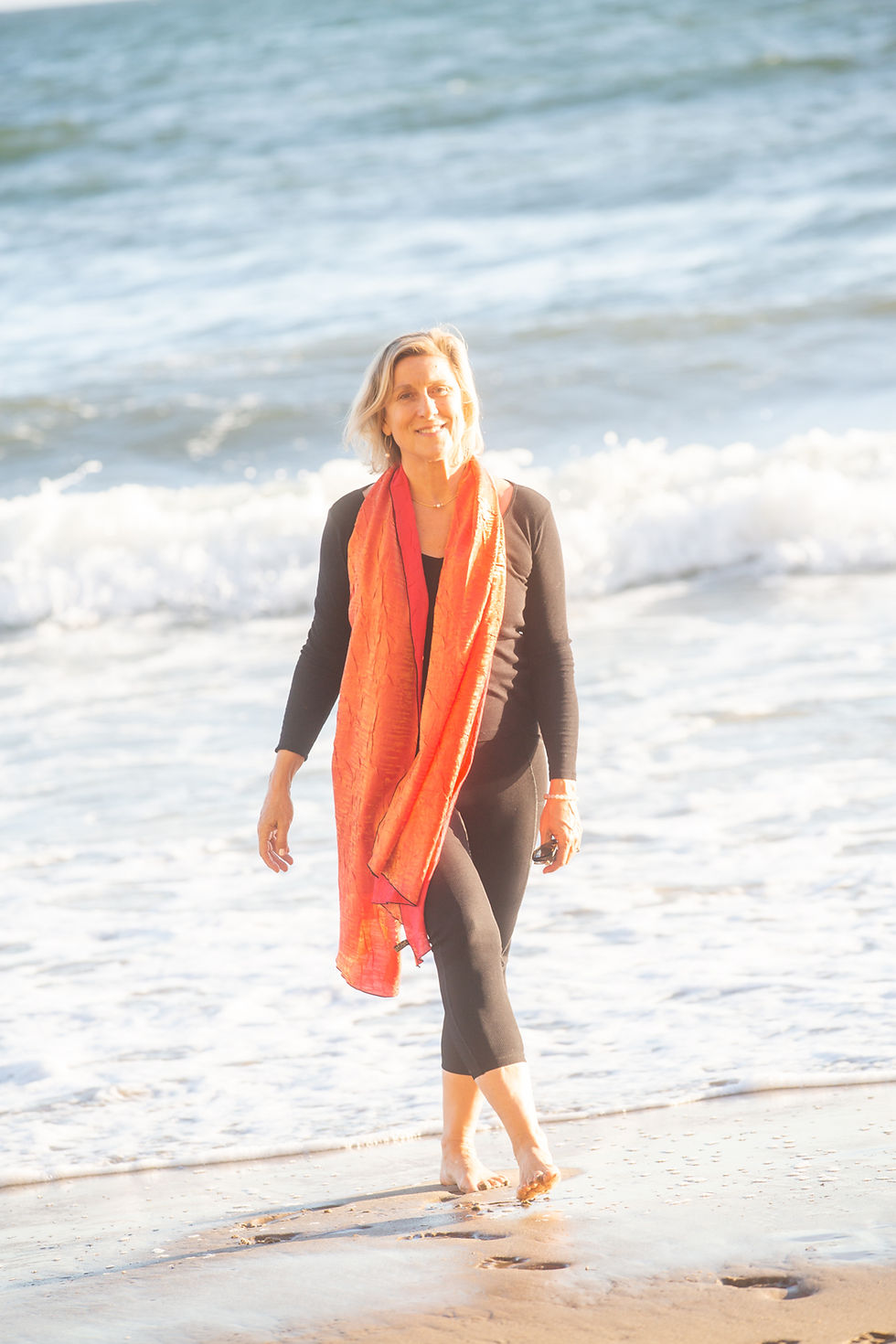 Petra Beumer walks barefoot on sunny beach, waves in the background. Bright, serene mood.