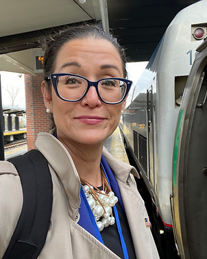 woman with glasses standing on a platform next to an Amtrak train.