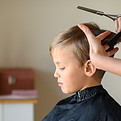 A young boy is getting a haircut, possibly at home or in a barbershop He wears a black hai