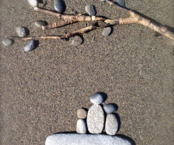 Three people composed of two rocks each, on a wet brown smooth sand background, with a twig horizontally underneath them and smaller rocks used as leaves on the twig for decoration