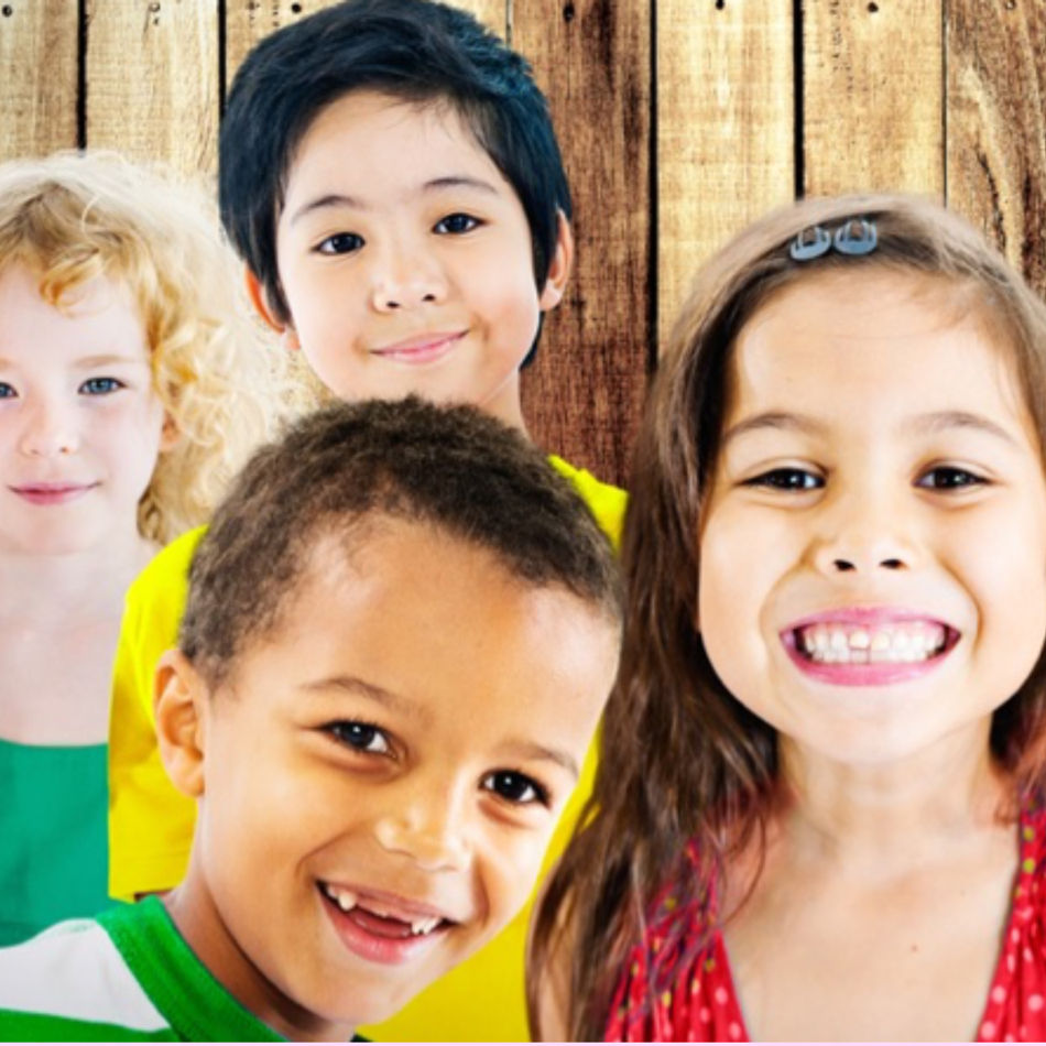 Four smiling children in colorful clothes stand against a wooden background, exuding a joyful and cheerful mood.