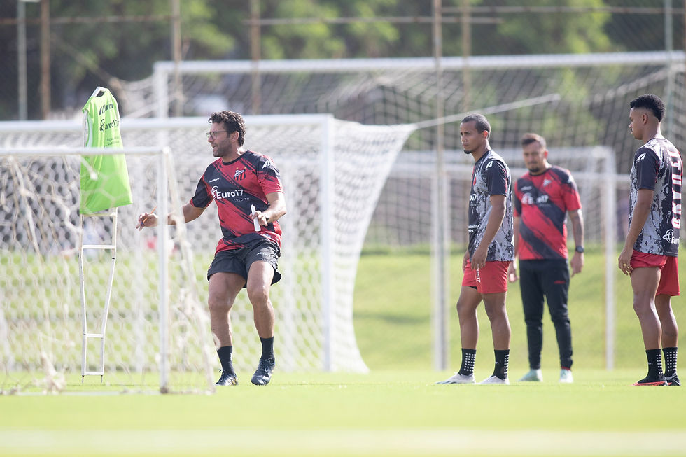 O técnico Alberto Valentim está dando instruções durante o treino aos jogadores. Tem dois jogadores e um auxiliar no canto direito da imagem olhando para o treinador