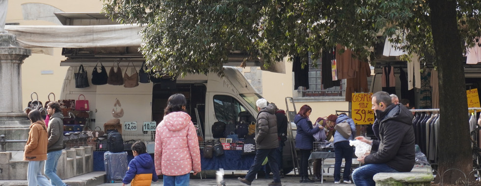 Locals and tourists mingle at an outdoor market in Florence, with children watching pigeons.