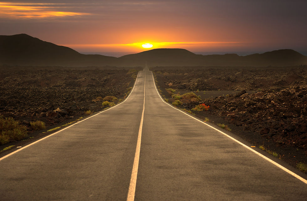 Strada diritta che attraversa un paesaggio scuro verso il sole basso sull'orizzonte