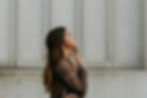 Woman in brown sweater gazes upward with a contemplative expression, set against a textured gray wall background.