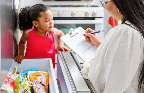 Mom and daughter are at the freezer making a grocery list.