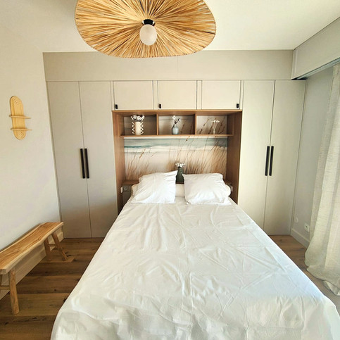 Chambre sur-mesure à Arcachon avec meuble intégré, suspension en fibres naturelles, sol effet chêne clair et ambiance sable et lin – projet de décoration intérieure pour location saisonnière.