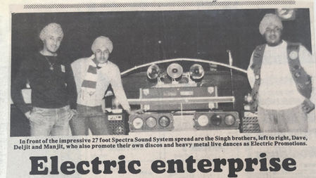 Black and white newspaper article with three young Sikh men standing in front of a mobile disco, all wearing jumpers, jeans and turbans. The headline says Electric Enterprise. The photo description says "In front of the impressive 27-foot Spectra Sound System spread area the Signh brothers, left to right, Dave, Deljit and Manjit, who also promote their own discos and heavy metal live dances as Electric Promotions.