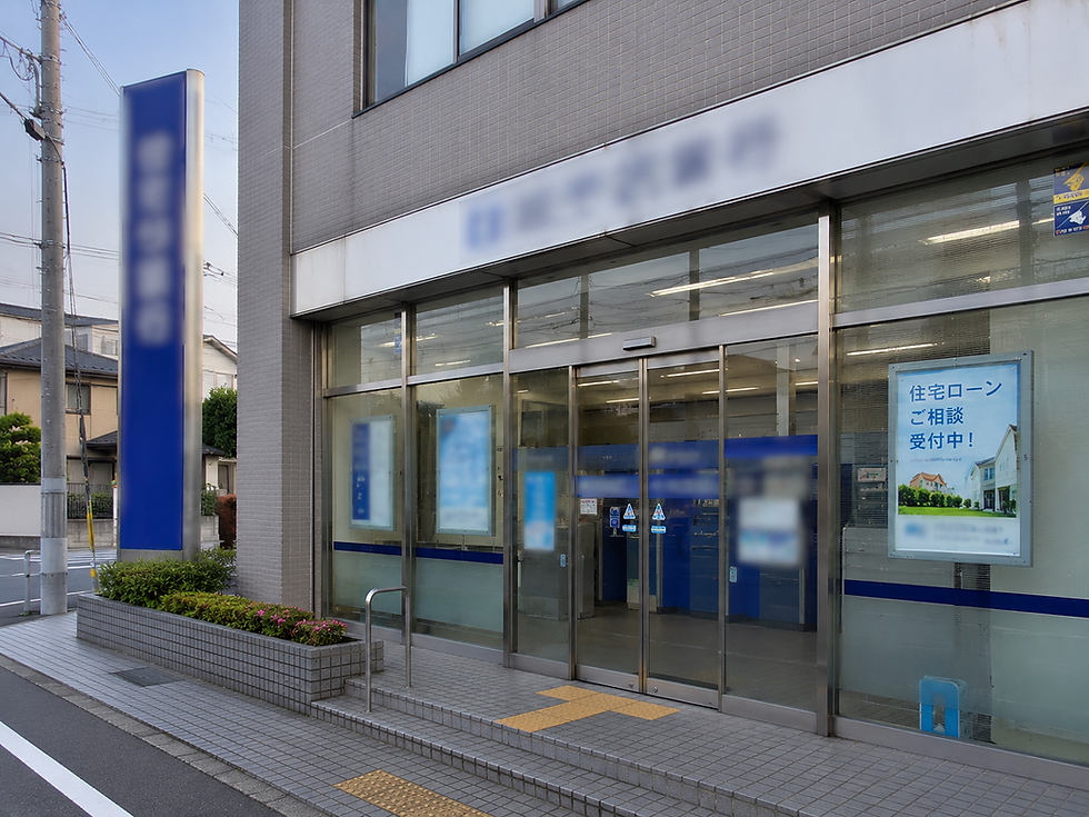 Japanese bank exterior with glass doors and blue signs; poster reads 住宅ローンご相談受付中! on a quiet street.