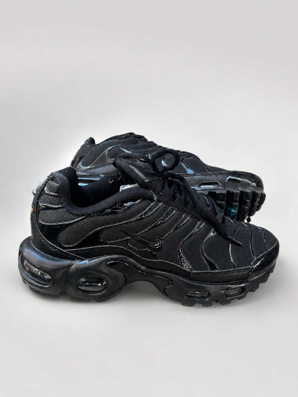 Thumbnail: Black Nike Air Max Plus men's shoes highlighting glossy TPU overlays and visible Tuned Air cushioning