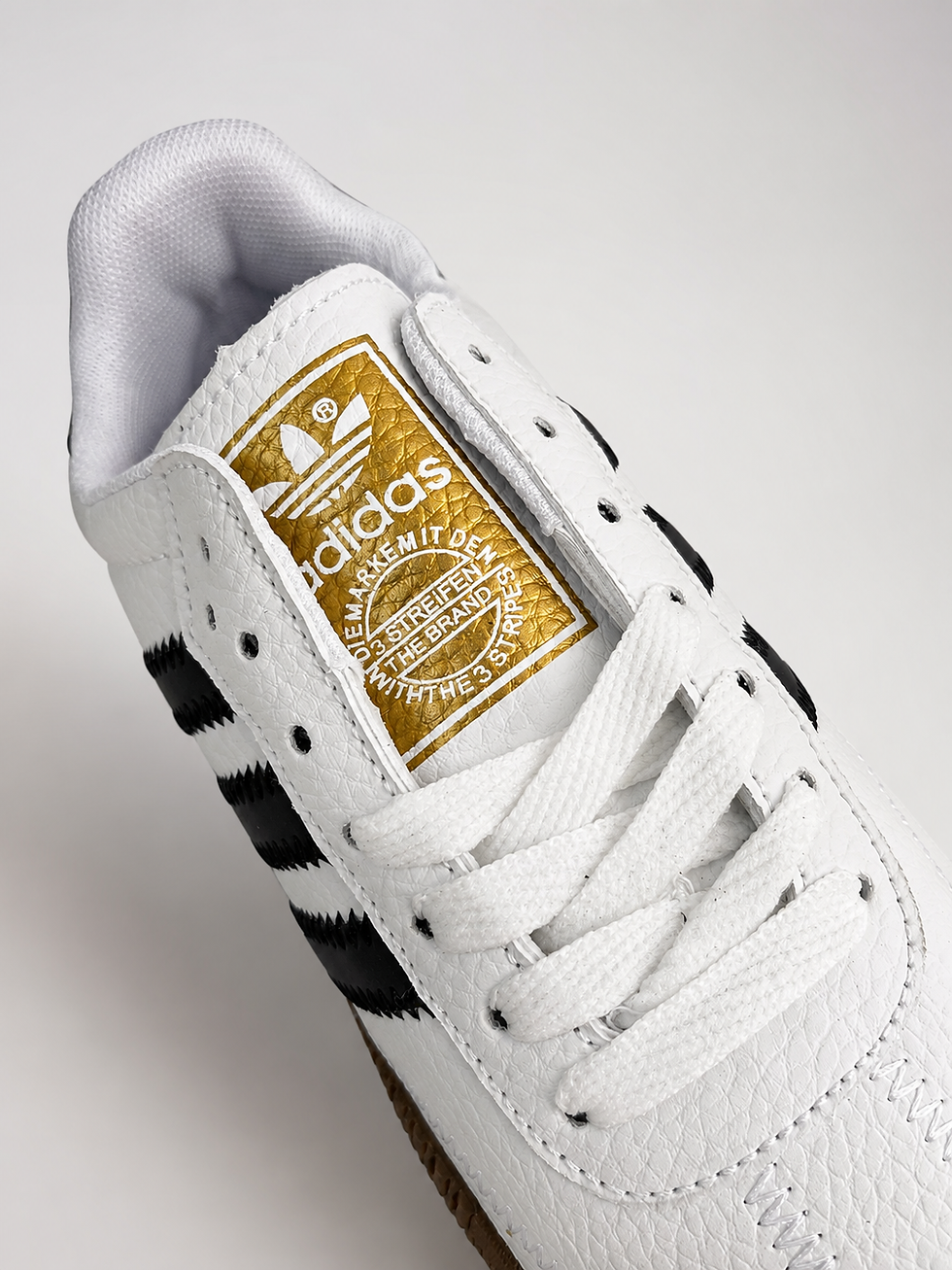 Thumbnail: Close-up of adidas Sambarose sneaker tongue featuring the gold adidas Originals logo and white leather upper.