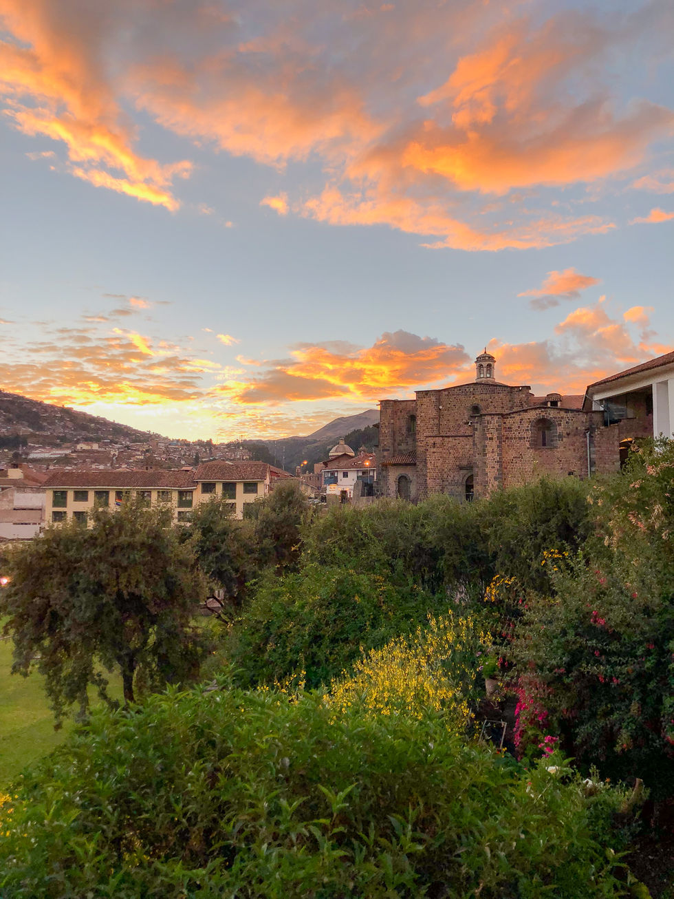 Orange clouds and blue sky at sunset with green bushes and old, stone buildings in Cusco, Peru — travel photography by Shutter & Sojourn