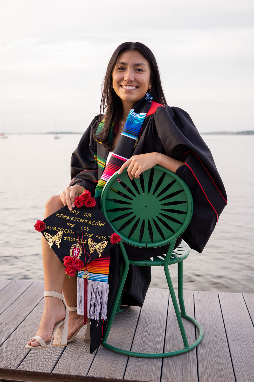 latina graduate sitting on memorial union terrace chair holding decorated cap High school senior boy looking off into the distance in green field — graduation photography by Shutter & Sojourn