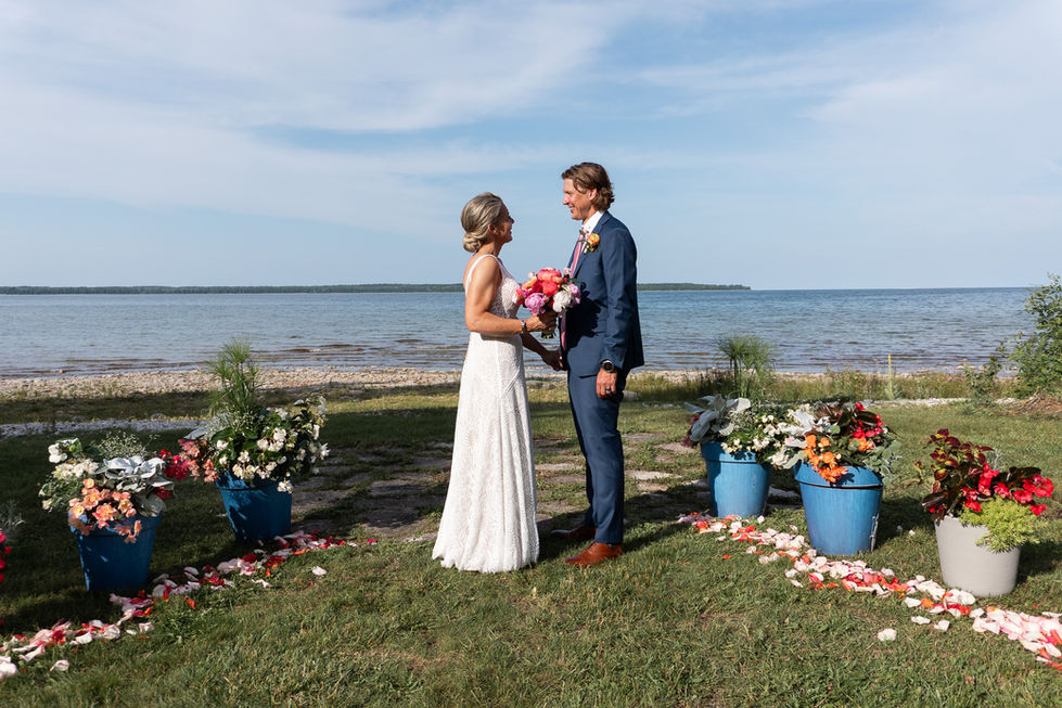 bride and groom candid photo talking with flowers around them in front of lake — wedding photography by Shutter & Sojourn
