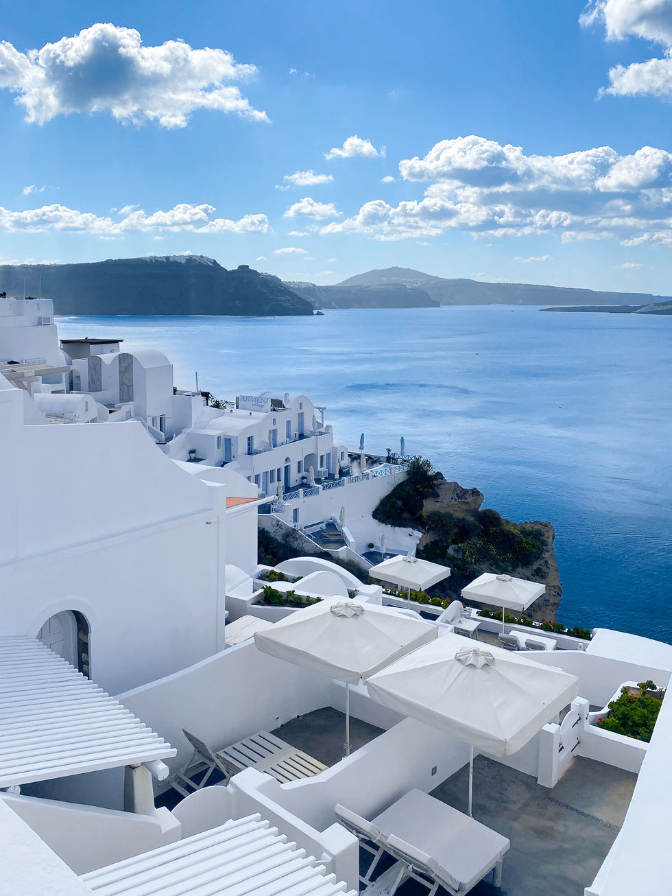 white buildings with umbrellas and patios down the hillside on Santorini — travel photography by Shutter & Sojourn