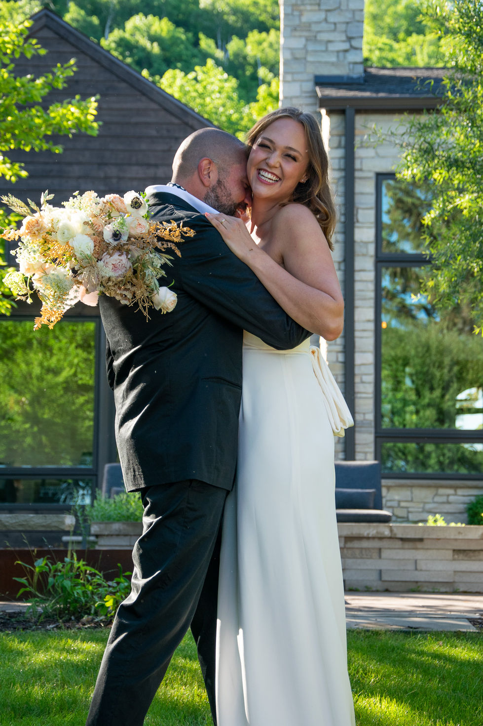 groom kissing bride's shoulder while she laughs in front of lake cottage in Wisconsin — wedding photography by Shutter & Sojourn