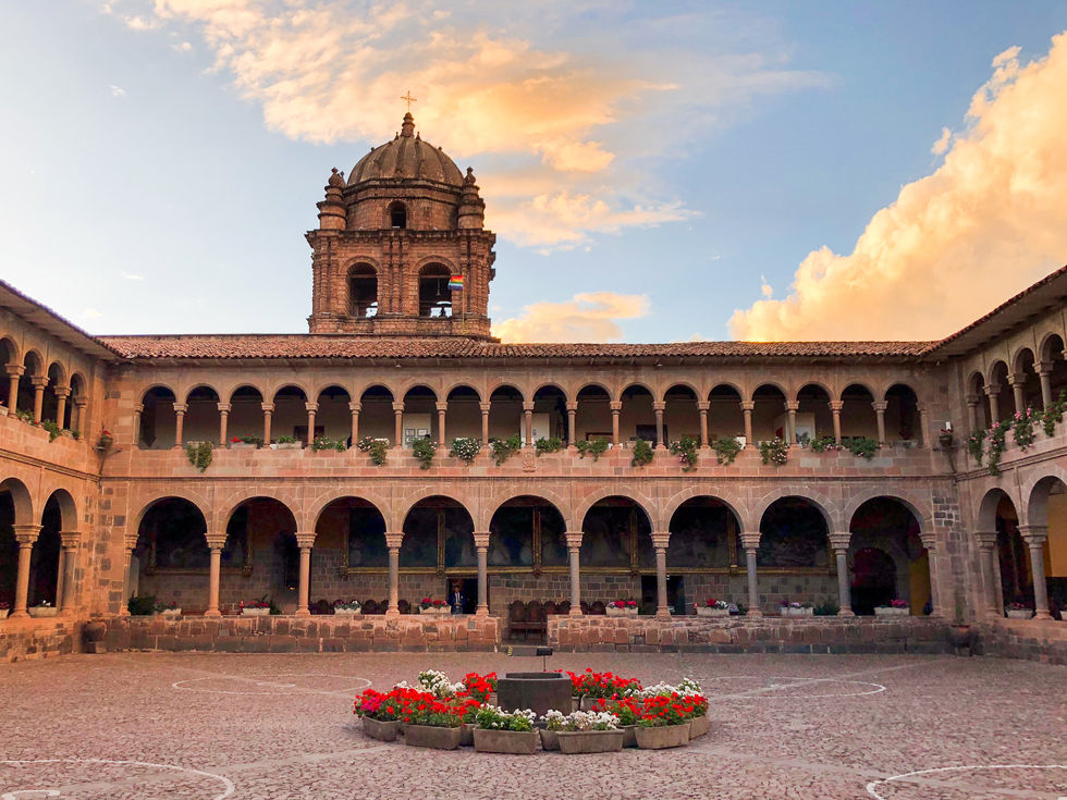 Stone courtyard with red and white flowers in the center and arched windows surrounding it in Cusco, Peru — travel photography by Shutter & Sojourn