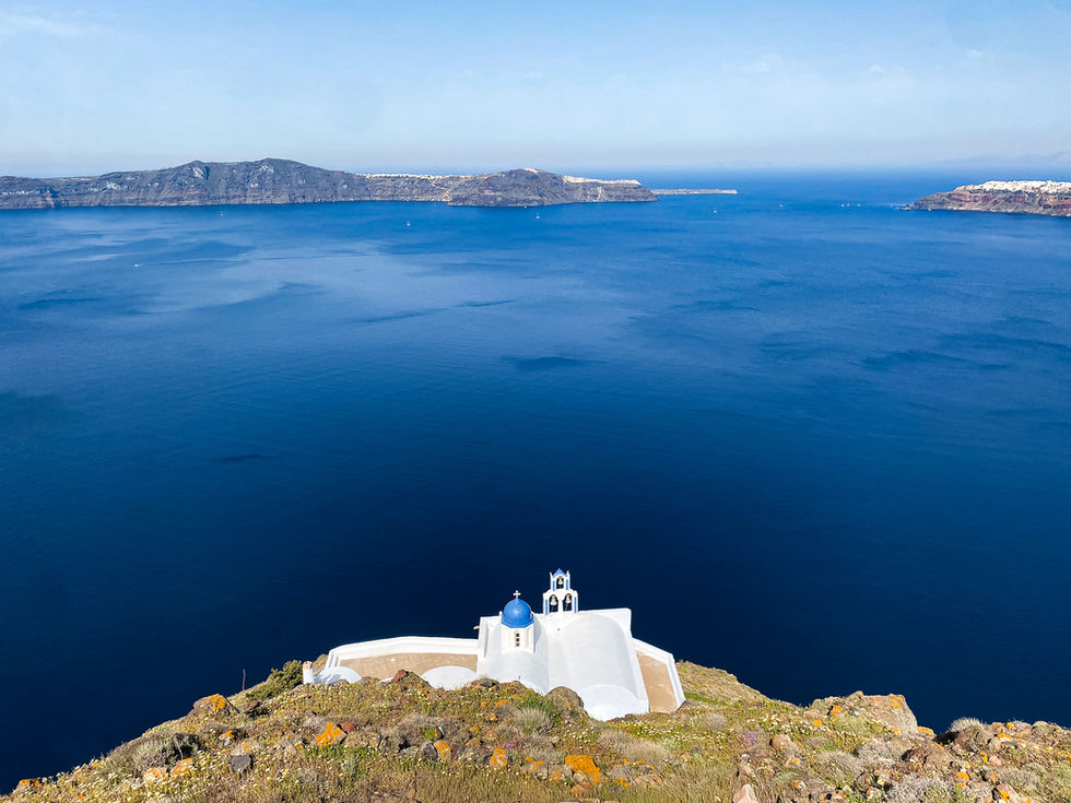 small, white church with bright blue dome roof at the edge of a cliff overlooking the blue sea on a Greek Island — travel photography by Shutter & Sojourn