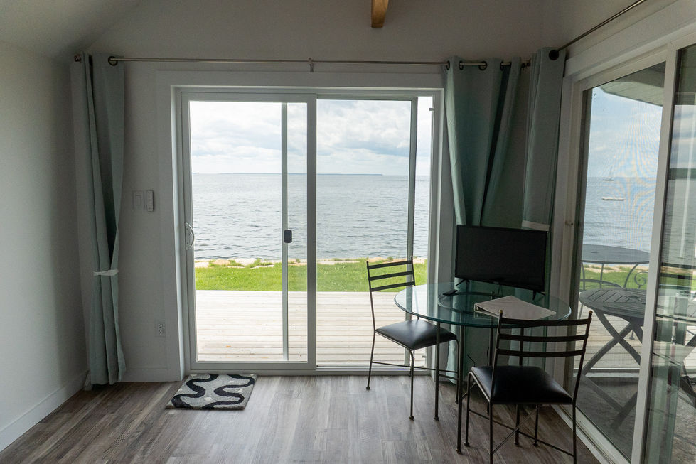 small table with tv and 2 black chairs next to balcony doors overlooking a lawn leading to Lake Michigan — real estate photography by Shutter & Sojourn