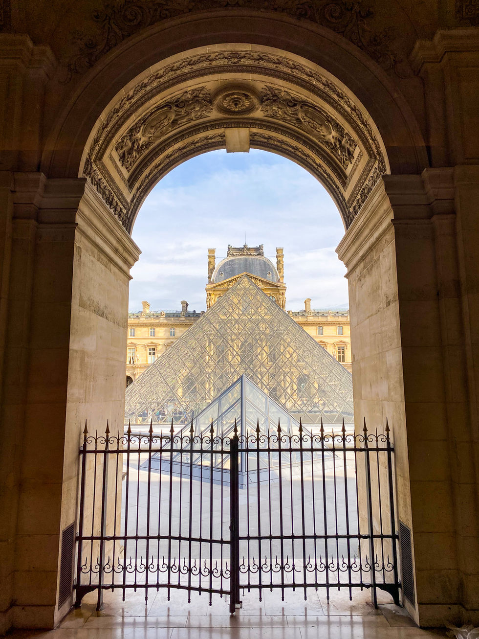 gated stone archway looking over the courtyard of the Louvre with glass triangle building in center — travel photography by Shutter & Sojourn