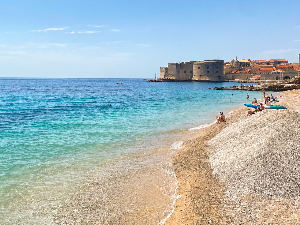 bright blue Mediterranean Sea leading to the old town of Dubrovnik with people sitting on the beach and kayaks — travel photography by Shutter & Sojourn