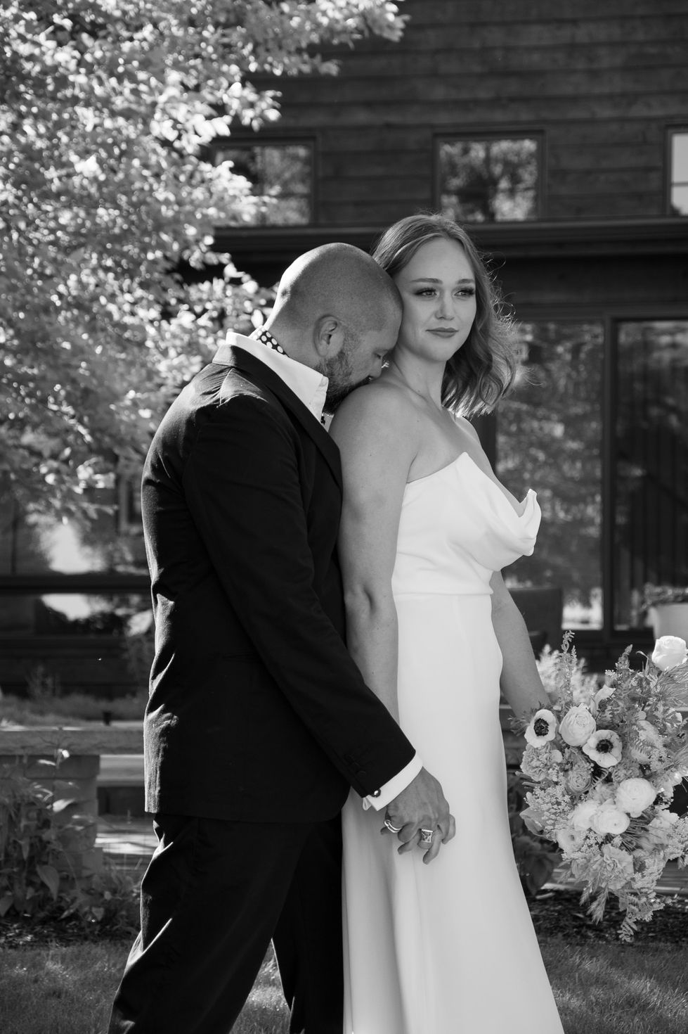 groom hugging bride from behind and kissing her shoulder in b&w — wedding photography by Shutter & Sojourn
