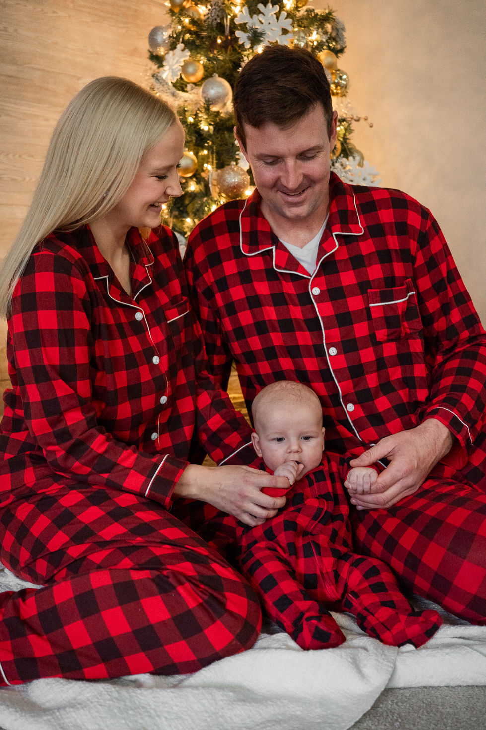 family sitting on floor in front of Christmas tree with newborn baby wearing matching outfits — family photography by Shutter & Sojourn