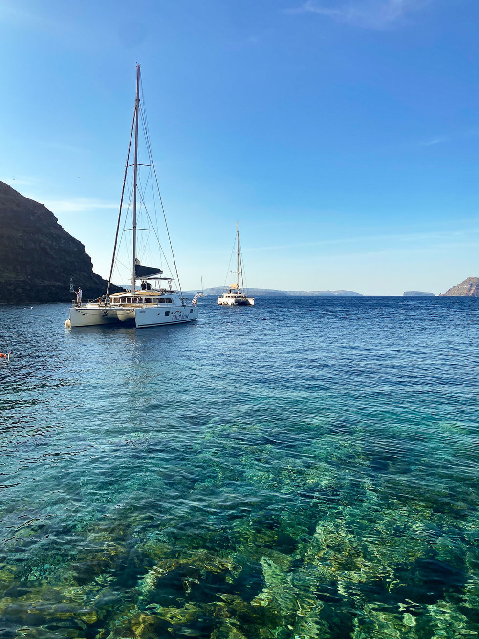 clear, blue and green water with rocks on sea floor and catamaran sailboats