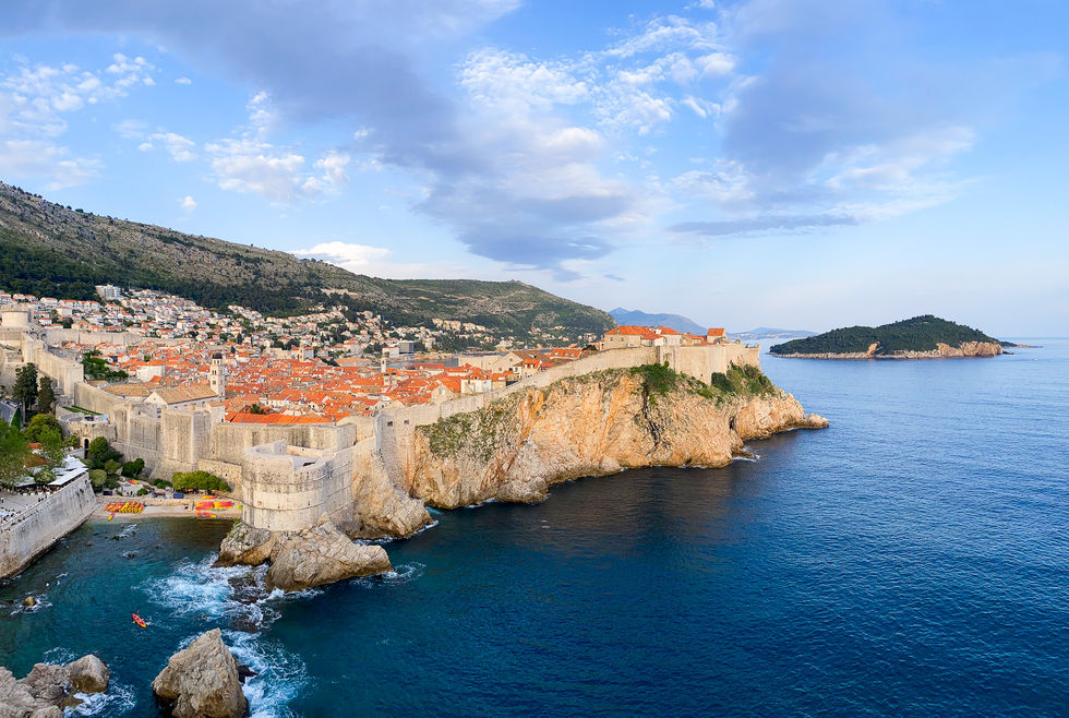 Landscape of entire city walls of Old Town Dubrovnik with small, kayak filled beach — travel photography by Shutter & Sojourn