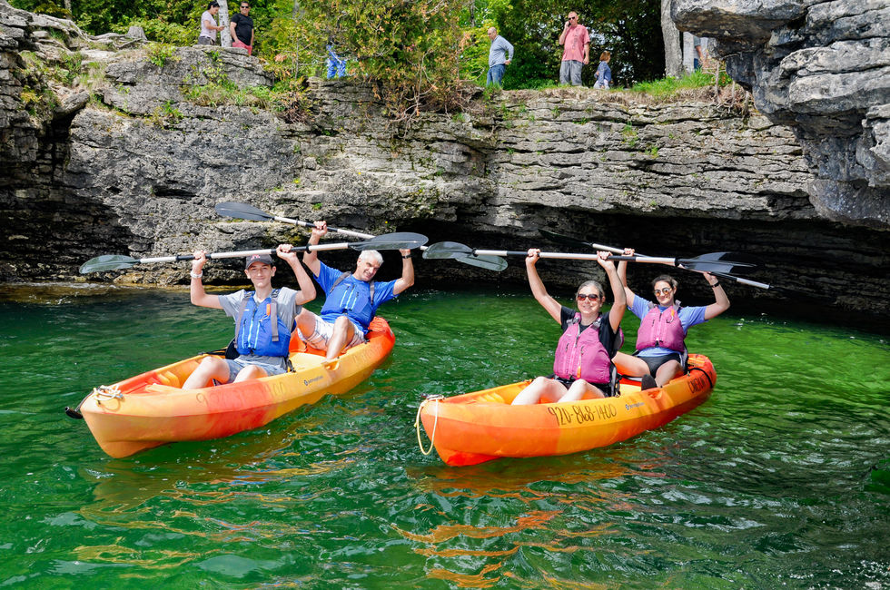 group of 4 kayakers holding paddles over their heads an smiling in front of cliffs on Lake Michigan — tour photography by Shutter & Sojourn
