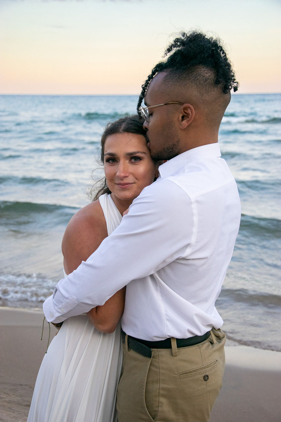 biracial bride and groom embracing each other while groom kiss's brides head and she looks into the camera — wedding photography by Shutter & Sojourn