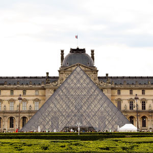 glass triangle of the Louvre centered with stone carved building behind and green hedges in front — travel photography by Shutter & Sojourn