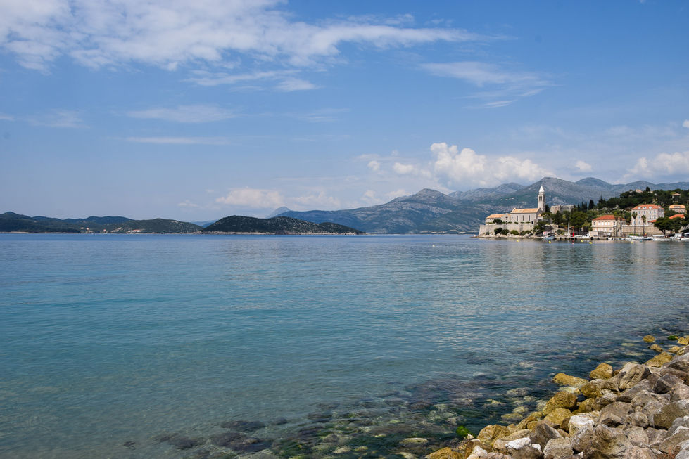 vibrant blue water with green and yellow rocks in foreground. Church steeple, mountains, and islands line the horizon — travel photography by Shutter & Sojourn